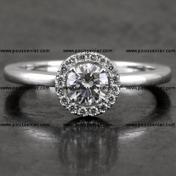 halo ring with a central briliant cut diamond surrounded by accent stones in castle pavé setting mounted on a bird-shaped or hollow V on a slightly convex band set with a small diamond on the side (compatible with a wedding ring)