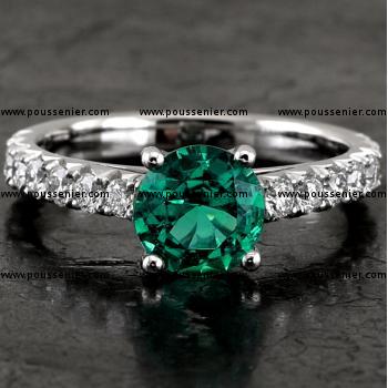 handmade solitaire ring with a brilliant cut emerald set with four prongs flanked by smaller brilliants on a band with palmettes set with fishtail finish