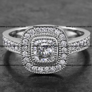 halo set ring with a cushion cut bezel set diamond surrounded by smaller brilliants flanked pavé set in boxes with millegrain finish wearable together with wedding band