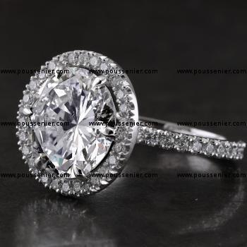 entourage ring met een grotere centrale briljant geslepen diamant met enkele V-constructie gemonteerd op een band een rechthoekig profiel voor drie vierde bezet met kleinere diamanten (samendraagbaar met trouwirng)