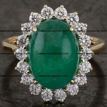 entourage ring with a central oval cabochon emerald surrounded by brilliant cut diamonds set with prongs