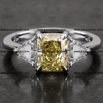 ring met een centrale fancy yellow of natuurlijk gele radiant geslepen diamant waarnaast twee trilliant geslepen diamanten