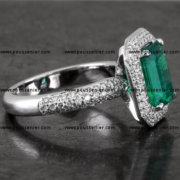 entourage halo ring with with a emerald cut emerald set with fine prongs on a single band castle pavé set with three rows of smaller brilliant cut diamonds