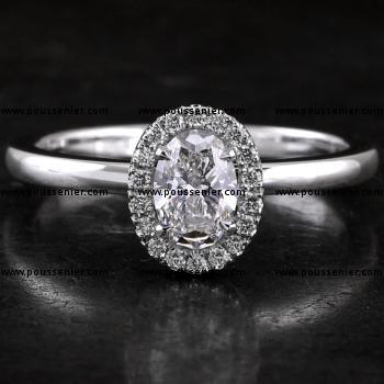 halo ring with a central oval cut diamond surrounded by castle pavé setting mounted on a bird-shaped or hollow V on a slightly convex band set with a small diamond on the side (compatible with a wedding ring)