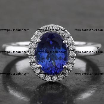 entourage ring with a central oval cut heated tanzanite surrounded by accent stones in castle pavé setting mounted on a bird-shaped or hollow V integrated in a slightly convex band set with a small diamond on the side (compatible with a wedding ring)