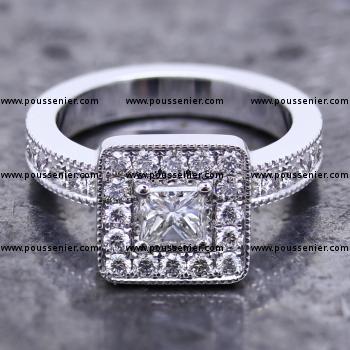 halo entourage ring with a central princess cut diamond with on the band pavé set brilliant cut diamonds finished with engraving and milligraine