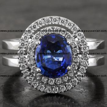 entourage ring with an oval cut heat treated sapphire surrounded by two rows of castle set brilliant cut diamonds mounted on an unset double band