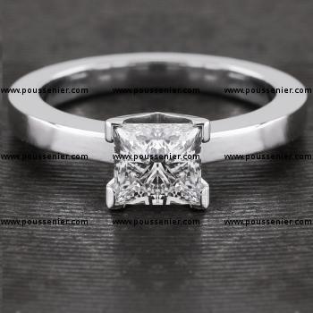solitairering met een princess geslepen diamant gezet in een strakke vierkante en iets hogere zetting gemonteerd tussen een iets smallere band