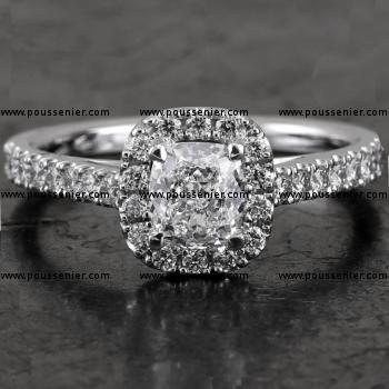 entourage or halo set ring with a central cushion cut diamond surrounded by smaller brilliant cut diamonds on the band with palmettes (V mounted slightly higher for a close matching wedding band)