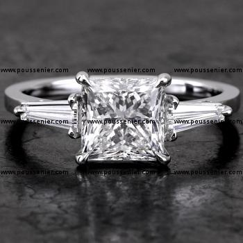 handgemaakte ring met een princess geslepen diamant geflankeerd door twee tapers gemonteerd op een fijnere band