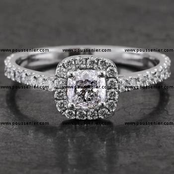  halo or entourage ring with a central cushion cut diamond surrounded with smaller brilliant cut diamonds on a castle-set band with palmettes between which a low mounted double V or pyramid shaped setting