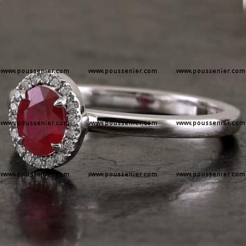 halo or entourage ring with a central oval ruby surrounded with a castle pavé setting mounted on a bird-shaped or hollow V integrated in a slightly convex band set on the side set with a diamond (can be combined with a wedding ring)